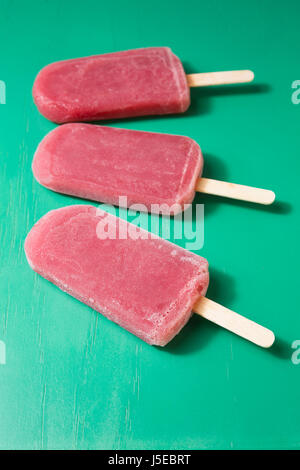 Three Homemade Raspberry and vanilla ice pops on a green wooden background. 3 strawberry or Raspberry icecream popsicles. Summer food. Stock Photo