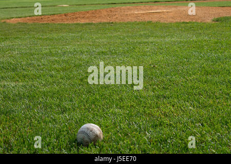 A  won baseball sits in the mown grass of a baseball diamond. Stock Photo