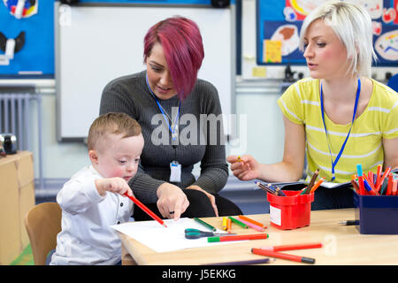 Nursery teacher sitting with a parent and her Down Syndrome son in the classroom. they are discussing the little boys progress. Stock Photo