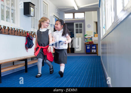Two female nursery students walking together down the corridor. One is holding a book and they are both laughing in conversation. Stock Photo