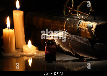 Vintage still life with candles near quill pen and books on dark background Stock Photo