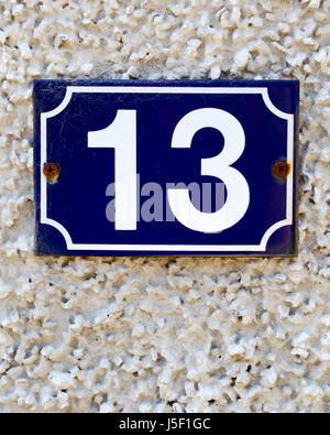 House number 13ca in white on a dark blue background, fastened to a pebble-dashed wall. Stock Photo
