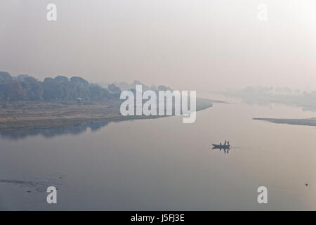 Viewed from a bridge above the river.A heavy morning mist shrouds the Yamuna River in Agra, India, in the distance local men fish from a small boat Stock Photo