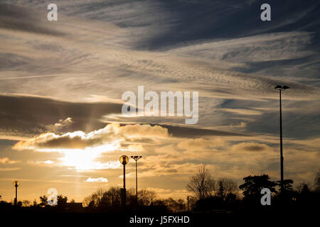 A shot of three lamp posts and a patterned sky taken just as the sun was setting, surrounding the environment with golden tones. Stock Photo