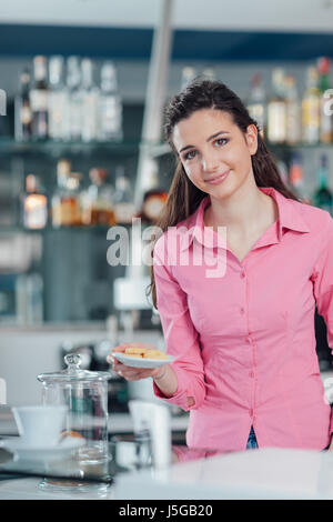 Young smiling barista serving cookies behind bar counter Stock Photo