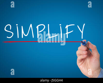 Businessman hand writing Simplify with marker on transparent wipe board isolated on blue. Stock Image Stock Photo