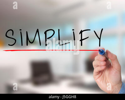 Businessman hand writing Simplify with marker on transparent wipe board isolated on office. Stock Image Stock Photo