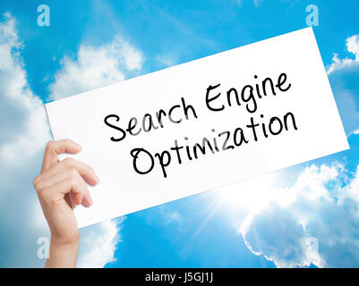 Search Engine Optimization Sign on white paper. Man Hand Holding Paper with text. Isolated on sky background.  Business concept. Stock Photo Stock Photo