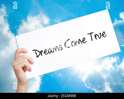 Dreams Come True Sign on white paper. Man Hand Holding Paper with text. Isolated on sky background.   Business concept. Stock Photo Stock Photo