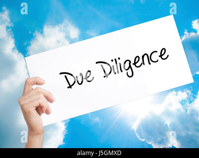 Due Diligence Sign on white paper. Man Hand Holding Paper with text. Isolated on sky background.  technology, internet concept. Stock Photo