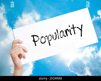 Popularity Sign on white paper. Man Hand Holding Paper with text. Isolated on sky background.  Business concept. Stock Photo Stock Photo