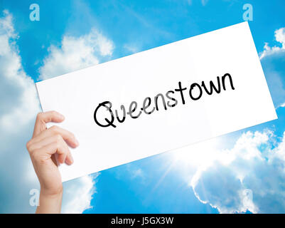 Queenstown  Sign on white paper. Man Hand Holding Paper with text. Isolated on sky background.   Business concept. Stock Photo Stock Photo