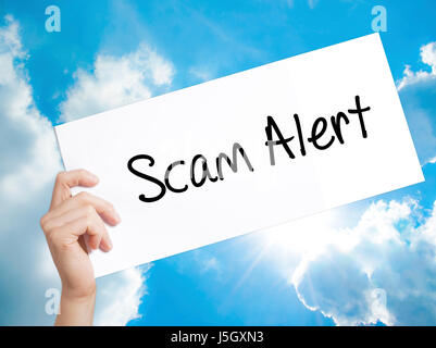 Scam Alert  Sign on white paper. Man Hand Holding Paper with text. Isolated on sky background.   Business concept. Stock Photo Stock Photo