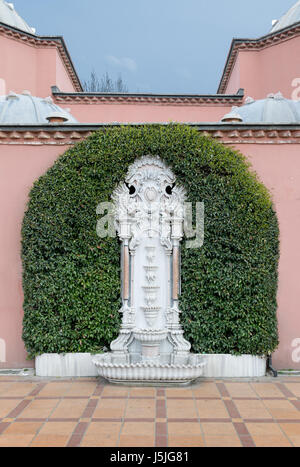 White marble sculpted wall fountain surrounded by green leaves over pink stone wall and tiled orange ceramic floor in Sultan Ahmed (Sultanahmet) squar Stock Photo
