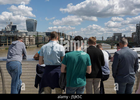 Young men stand on the Millennium Bridge to admire the views across the River Thames to the Walkie-Talkie building and Tower Bridge in City of London, on 14th May 2017, in London, England. Stock Photo