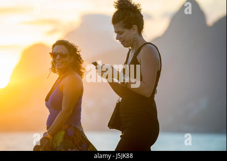 RIO DE JANEIRO - FEBRUARY 21, 2017: Young women walk along the boardwalk at Arpoador to enjoy the popular sunset view of Ipanema. Stock Photo