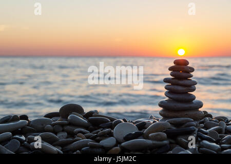 Cairn stones stacked with sun on the stony beach on sunset. Stock Photo