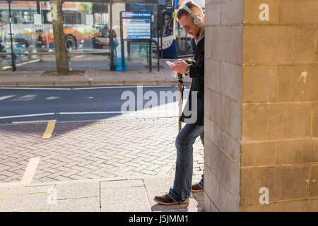 A man wearing headphones and using his mobile phone in Canterbury, Kent. Stock Photo