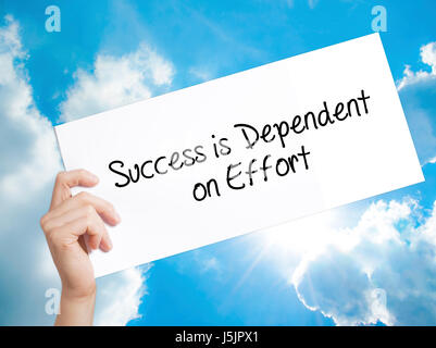 Success is Dependent on Effort Sign on white paper. Man Hand Holding Paper with text. Isolated on sky background.   Business concept. Stock Photo Stock Photo