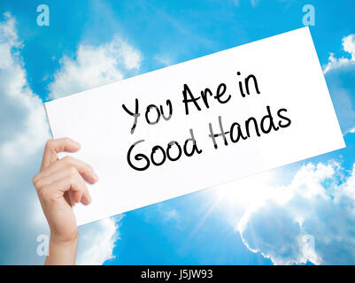 You Are in Good Hands Sign on white paper. Man Hand Holding Paper with text. Isolated on sky background.   Business concept. Stock Photo Stock Photo