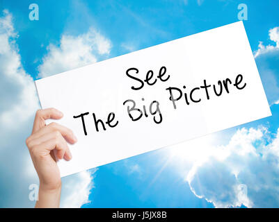 See The Big Picture Sign on white paper. Man Hand Holding Paper with text. Isolated on sky background.  Business concept. Stock Photo