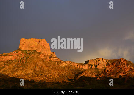 Storm clouds darken the sky in the east as the setting sun illuminates Casa Grande in the Chisos Mountain Range at Big Bend National Park in Texas Stock Photo