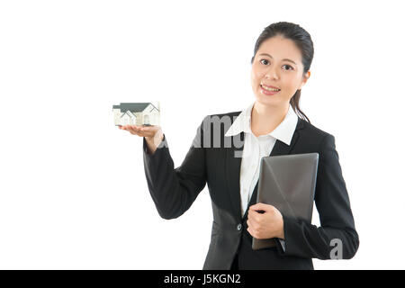 young building designer displaying new house miniature model over copyspace and using mobile digital tablet computer working connect with company on t Stock Photo