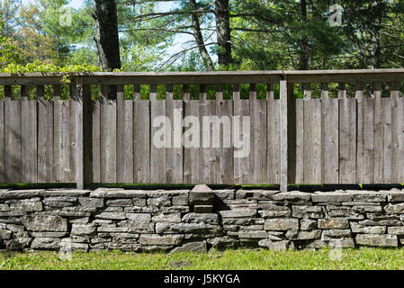 Section of Stacked Stone Wall with Grey Distressed Wood Fence in Country Setting . Grass in foreground and Trees in Background. Stock Photo