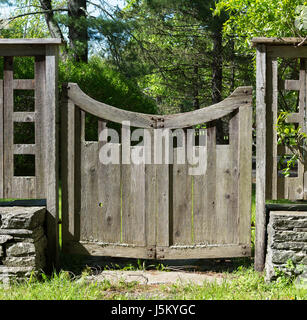 Distressed Grey Wood Gate with a Curved Top in Country Setting,  with Lichens  and Stacked Stone, Grass and Trees. Stock Photo