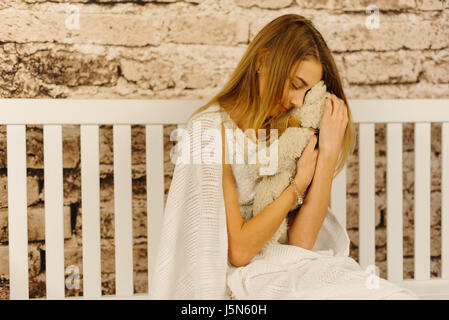 The lovely portrait portrait of the teenage girl hugging the teddy bear while sitting on the white bench. Stock Photo