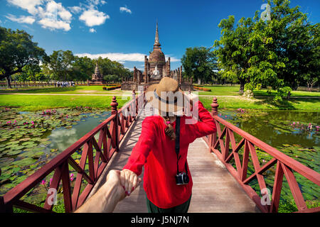 Tourist Woman in red shirt holding her husband by hand and going to ancient stupa in Sukhohai Historical Park, Thailand Stock Photo