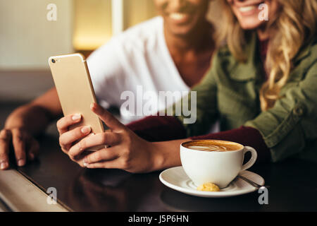 Close up of  young man and woman sitting together at cafe and taking selfie with mobile phone. Friends making selfie at coffee shop using smart phone. Stock Photo