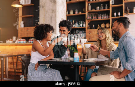 Young people sitting at cafe table and having coffee together. Group of friends making a toast with coffee. Stock Photo