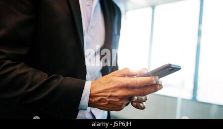 Close up of businessman using his mobile phone indoor.  Focus on male hands holding smart phone. Stock Photo