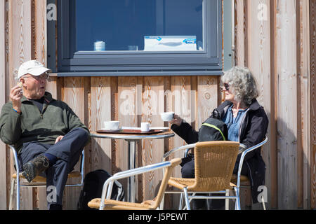Denbighshire, Wales, UK Weather – Warmer weather and sunshine over the North Wales including the coastal resort of Rhyl, Denbighshire. A couple enjoying the sunshine and afternoon tea outside a cafe along the promenade at Rhyl in North Wales Stock Photo