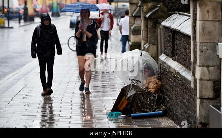 Brighton, UK. 18th May, 2017. A man asks for money under an umbrella on the pavement as people walk past in torrential rain in central Brighton today Credit: Simon Dack/Alamy Live News Stock Photo