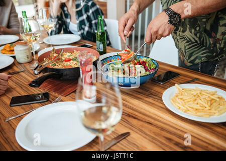 Closeup of man mixing vegetable salad and having dinner with friends at home Stock Photo