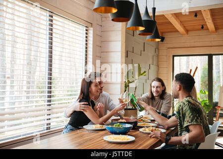 Group of cheerful young friends giving toasts and clinking glasses on the kitchen Stock Photo