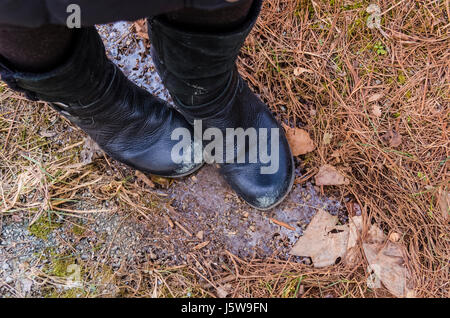 Macro closeup of frozen iced icicle on forest ground in winter with women's black leather boots Stock Photo
