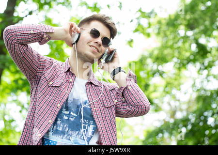 Handsome young man enjoys listening to music outdoors. Selective focus and small depth of field. Stock Photo