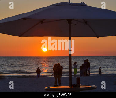The sunset with the silhouette of an umbrella and people on the beach. This is at Indian Rocks Beach, Gulf of Mexico, Florida Stock Photo