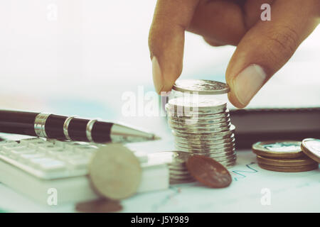 Hand putting coin on stack of coins with calculator and pen Stock Photo