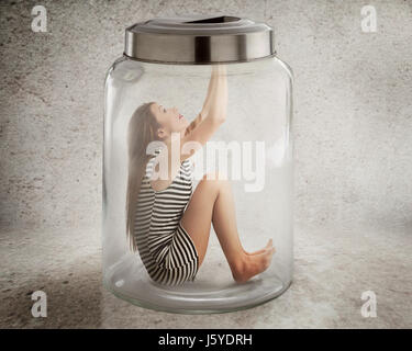 Lack, violation of human rights liberty. Young lonely woman sitting in glass jar isolated grey wall background. Suppression of freedom, restrain, empl Stock Photo