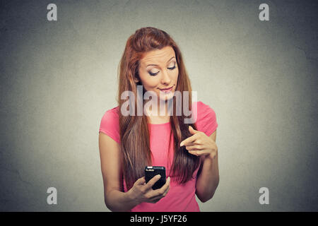 Portrait young angry woman unhappy, annoyed by something, someone on her cell phone while texting, receiving bad sms text message isolated grey wall b Stock Photo