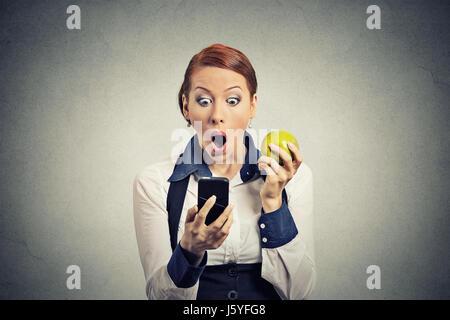 Closeup portrait anxious shocked young business woman looking at phone seeing bad news or photos with disgusting emotion on her face isolated grey wal Stock Photo