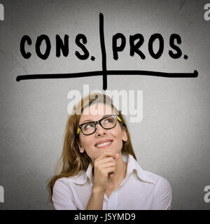 pros and cons, for and against argument concept. Thinking young business woman with glasses looking up isolated on grey wall background. Face expressi Stock Photo