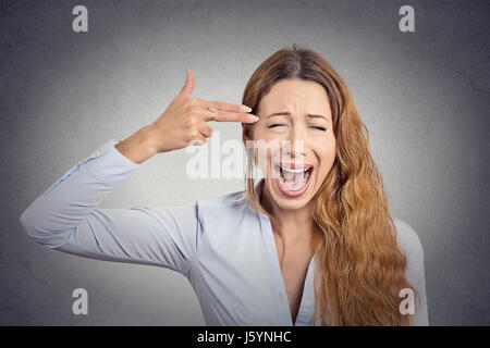 Portrait stressed young woman with hand gun gesture screaming isolated on grey wall background. Negative human emotions face expression feelings life  Stock Photo