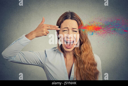 Headshot portrait young woman committing suicide with finger gun gesture, explosion of colors isolated on grey wall background. Human emotions face ex Stock Photo