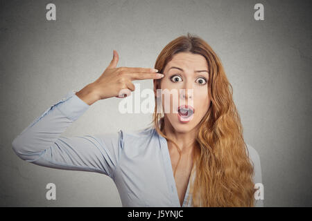 Portrait stressed young woman with hand finger gun gesture shocked wide open mouth isolated on grey wall background. Negative human emotions face expr Stock Photo