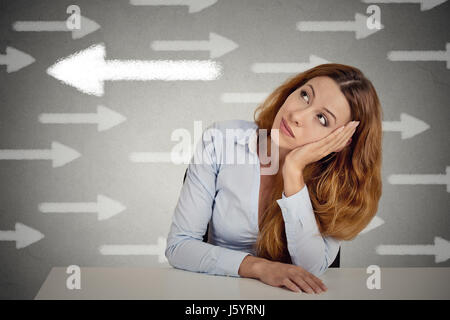 Thoughtful woman taking a chance going against flow. Thoughtful businesswoman sitting at table isolated on grey wall office background. Counterbalance Stock Photo